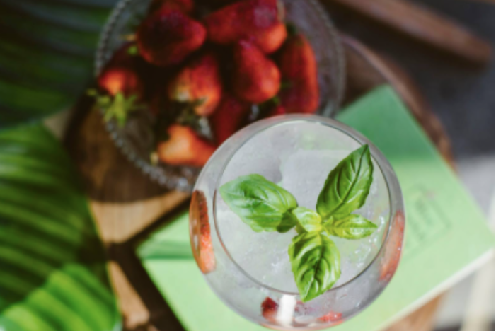 Cocktail with basil garnish and bowl of strawberries
